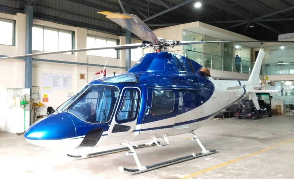 A blue and white helicopter with a metallic blue nose and white fuselage, parked in a hangar.