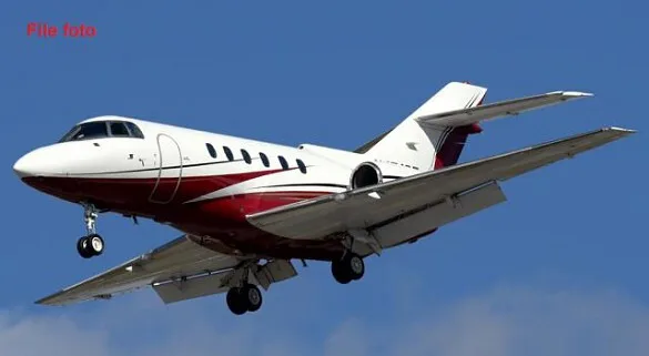 A white and red business jet with landing gear extended, flying against a blue sky.