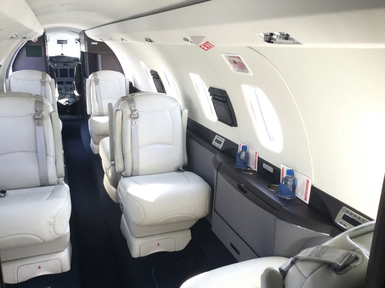 Aircraft cabin with light gray leather seats and a view towards the cockpit.