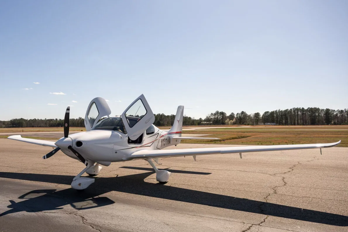 A white Cirrus SR22 aircraft with red and black accent stripes, tail number N131VA, parked on an airfield with both doors open.