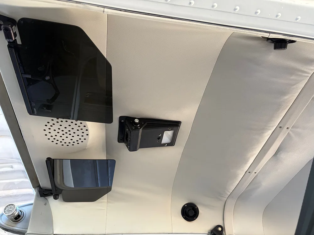 The light-colored ceiling and side panel of the aircraft cabin with a speaker and sun visors.