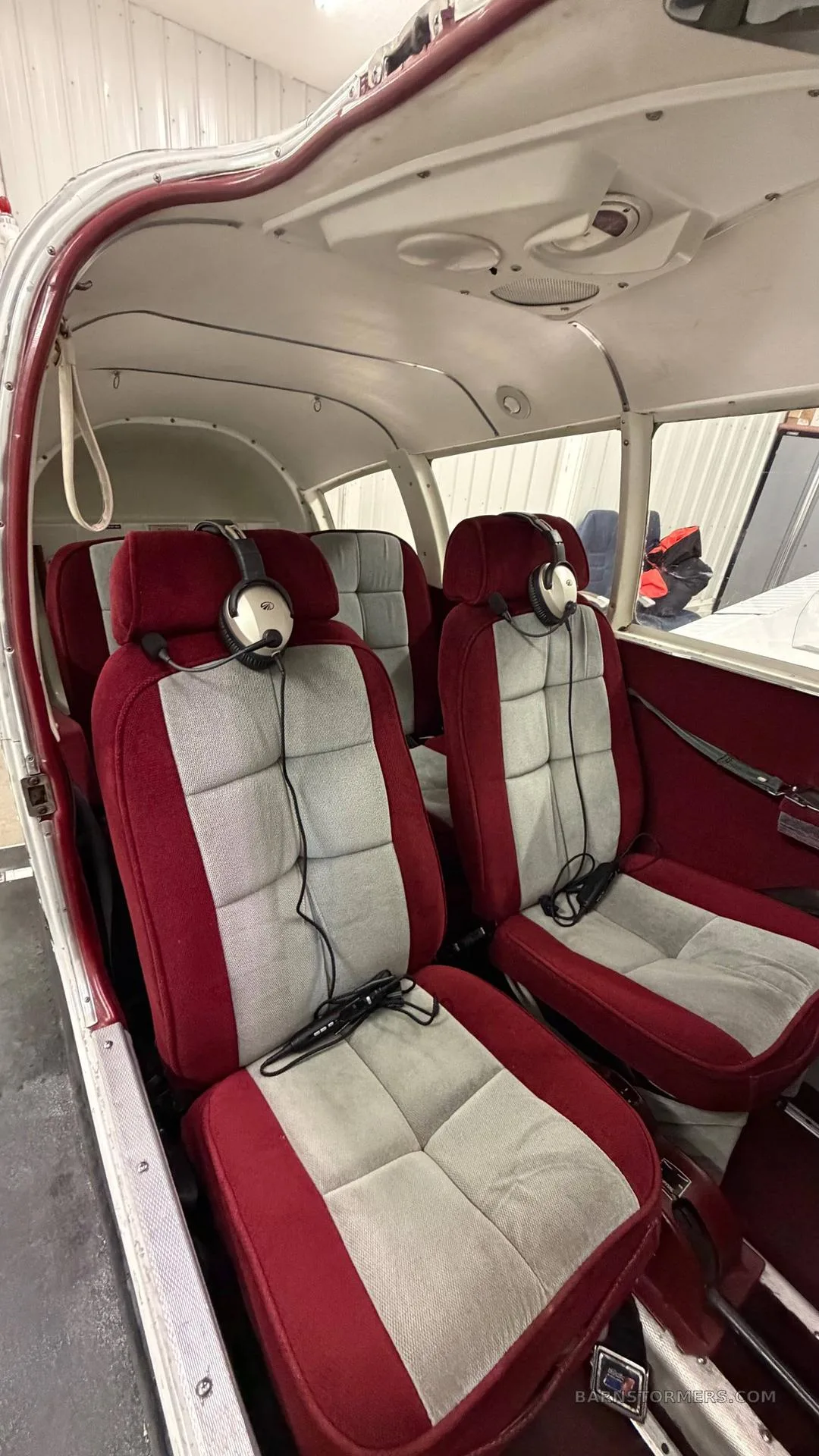 The interior cabin of a small aircraft with four red and grey upholstered seats, each with a headset.