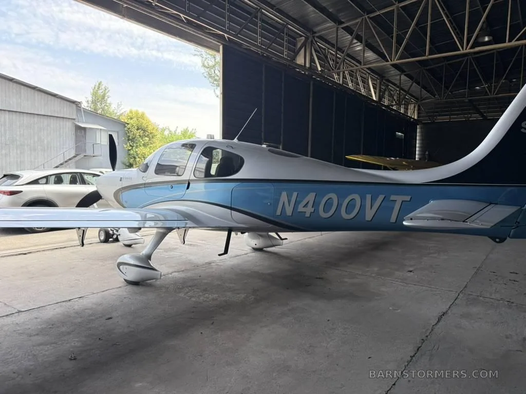 A white and blue Cirrus SR22 aircraft, registration N400VT, is parked inside a hangar with its door open.