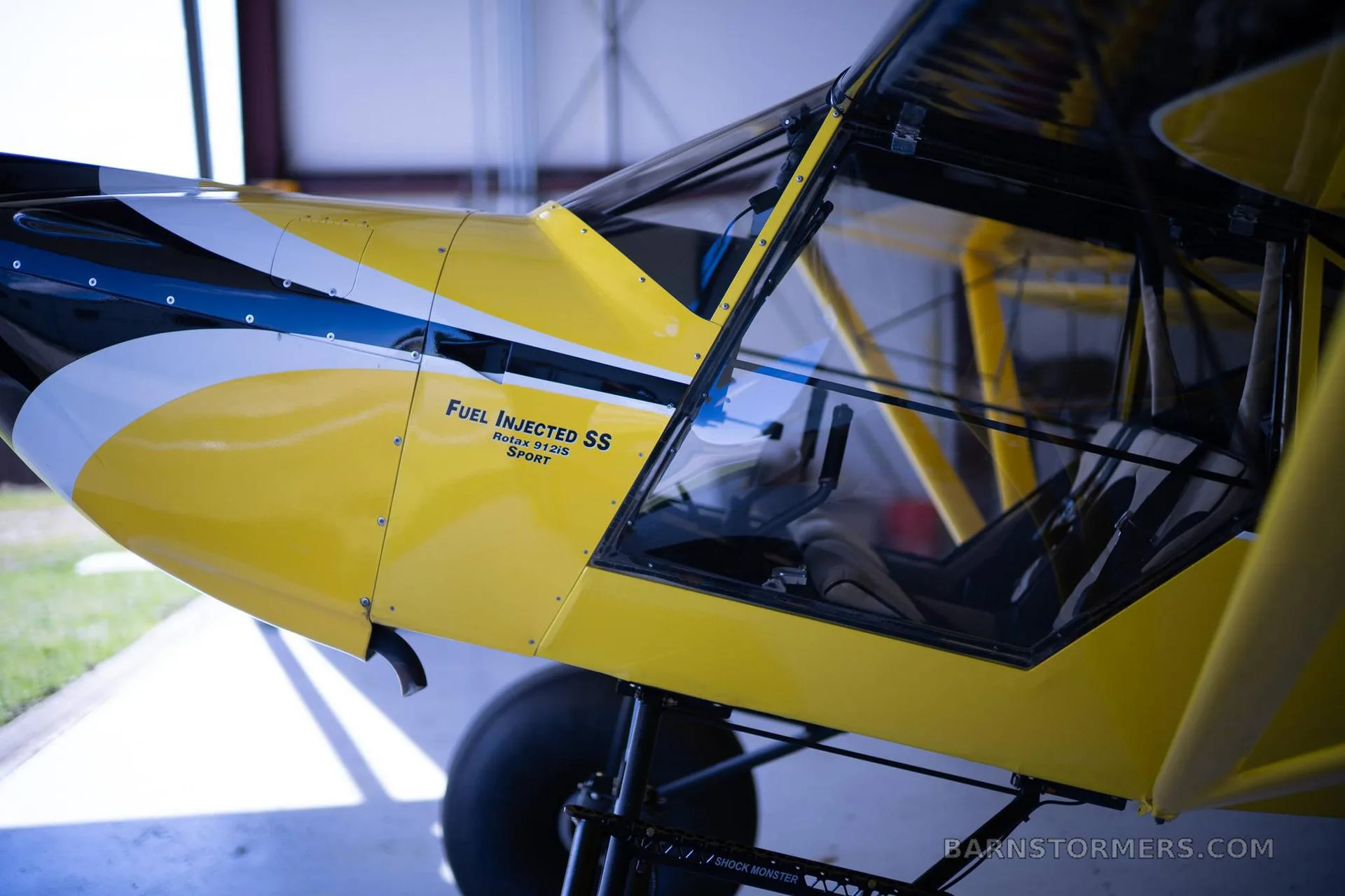 A close-up side view of the yellow and black Kitfox aircraft's fuselage and cockpit area inside a hangar.