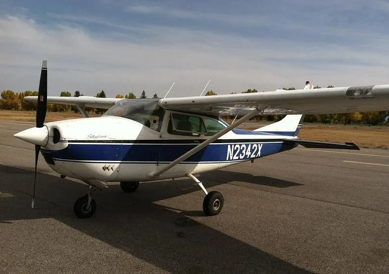 A white and blue Cessna Skylane N2342X parked on an asphalt runway under a partly cloudy sky.