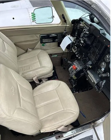 The aircraft's front cabin showing light-colored leather pilot and co-pilot seats and a partial view of the cockpit controls.