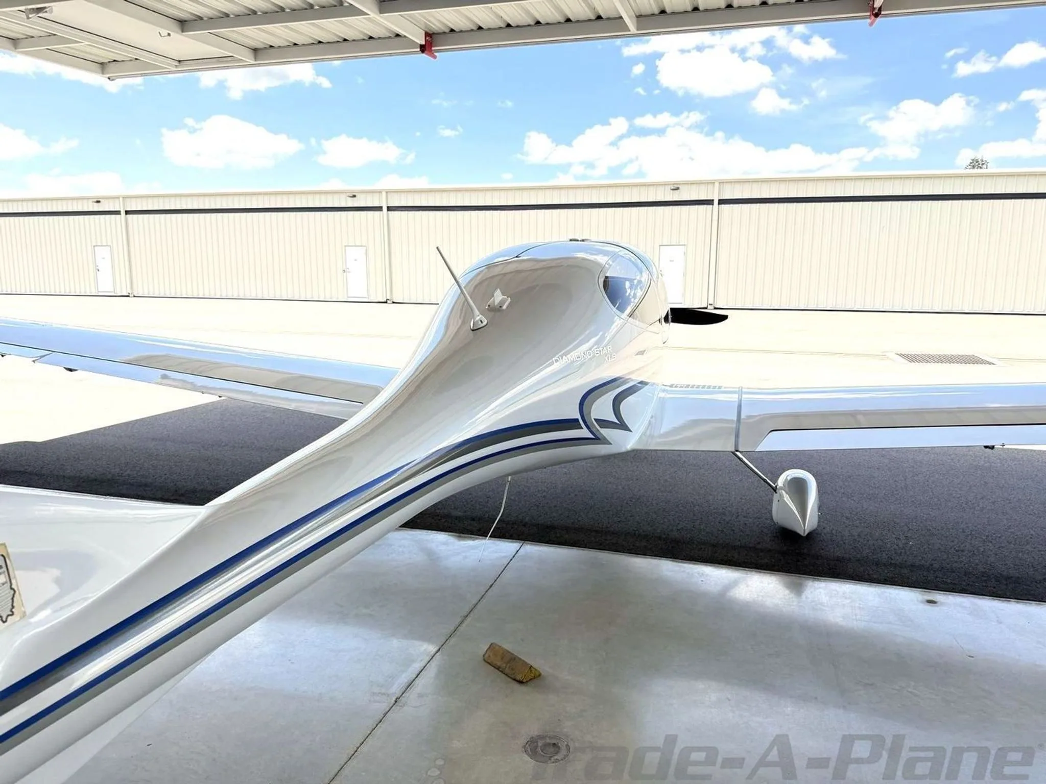 An overhead rear view of the fuselage and wing of a white Diamond Star DA40 XLS aircraft with blue and grey stripes.