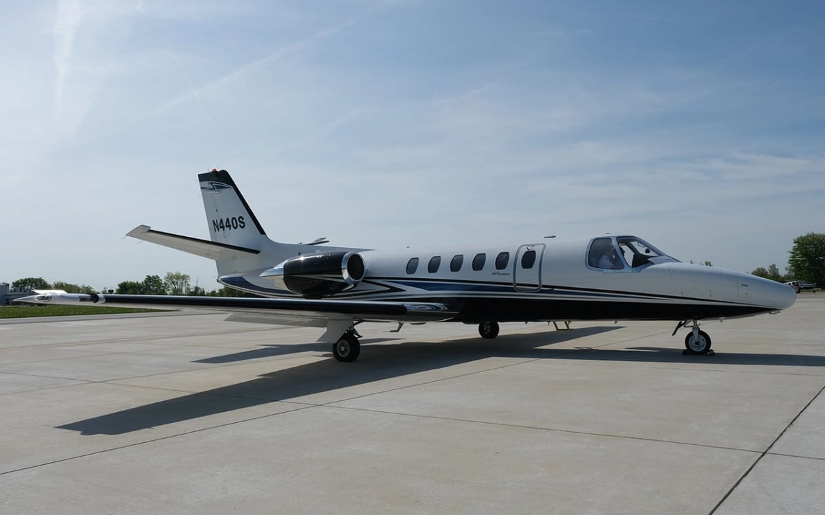 Side view of a white and black jet with blue accents, tail number N440S.