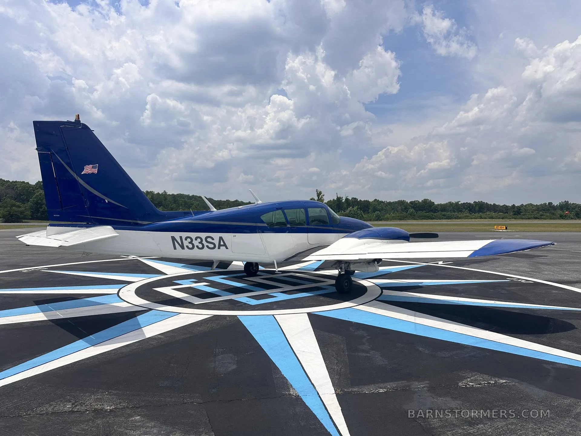 A side view of a blue and white single-engine aircraft (N33SA) parked on a compass rose marking on an airfield.