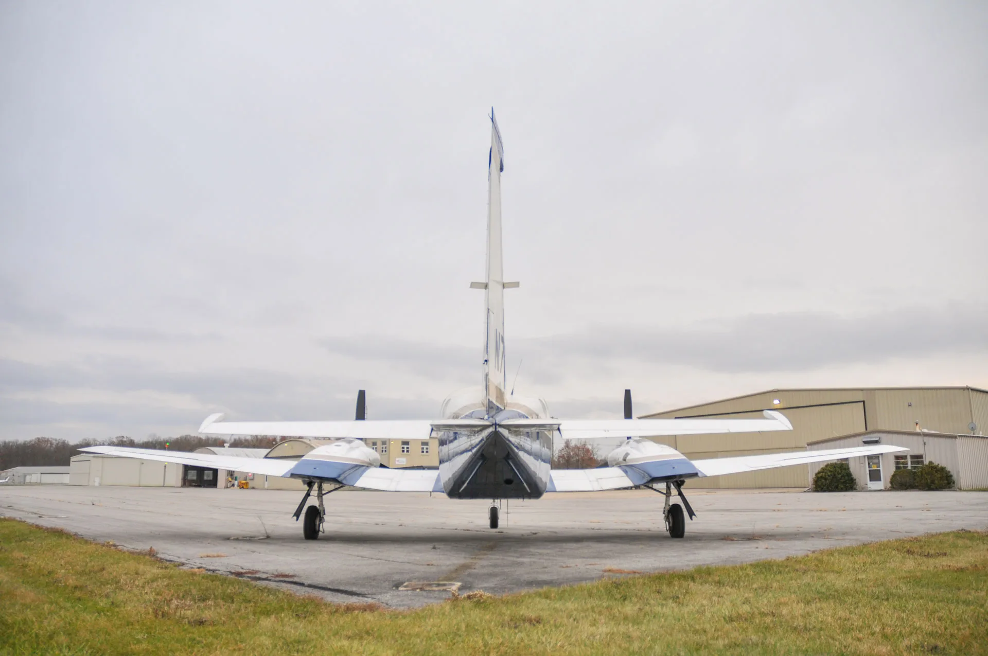 A rear view of the N721HB aircraft, a white and blue twin-engine plane, parked on an airfield.