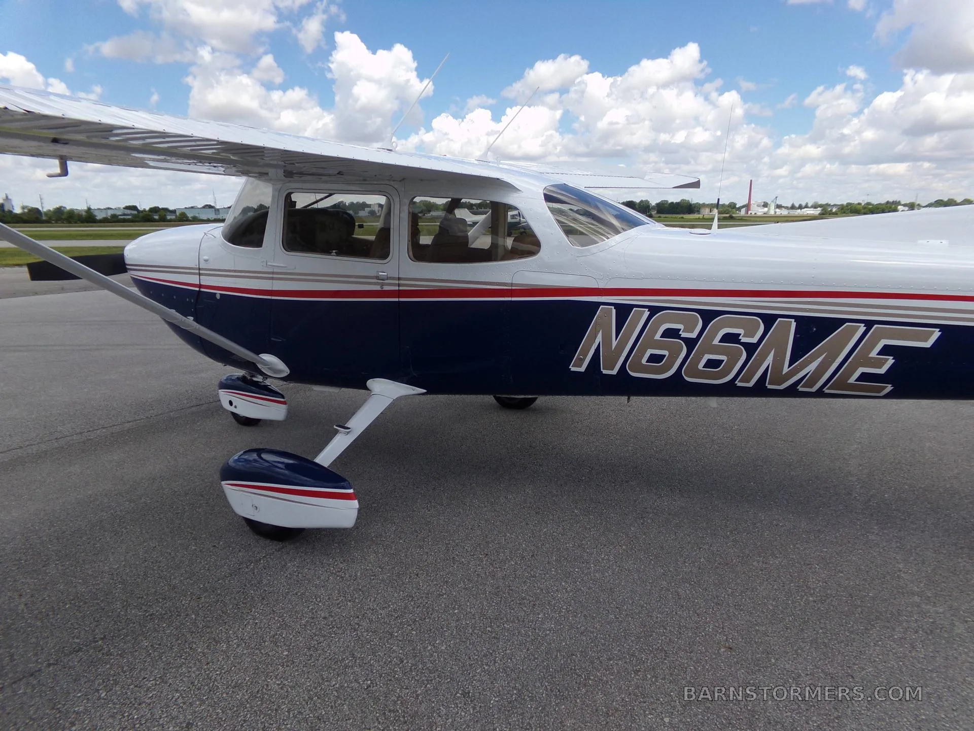 A close-up view of the fuselage and wing of a white and blue Cessna 172 Hawk XP with red and gold stripes, showing the N-number N66ME.