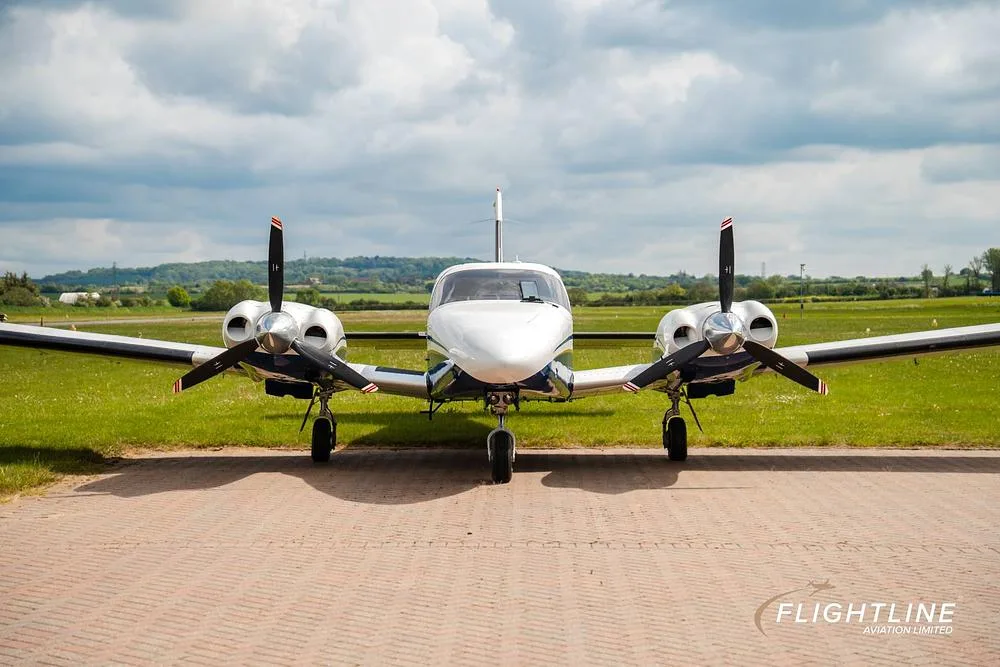 A head-on view of a white and blue twin-engine Piper Seneca aircraft parked on a tarmac.