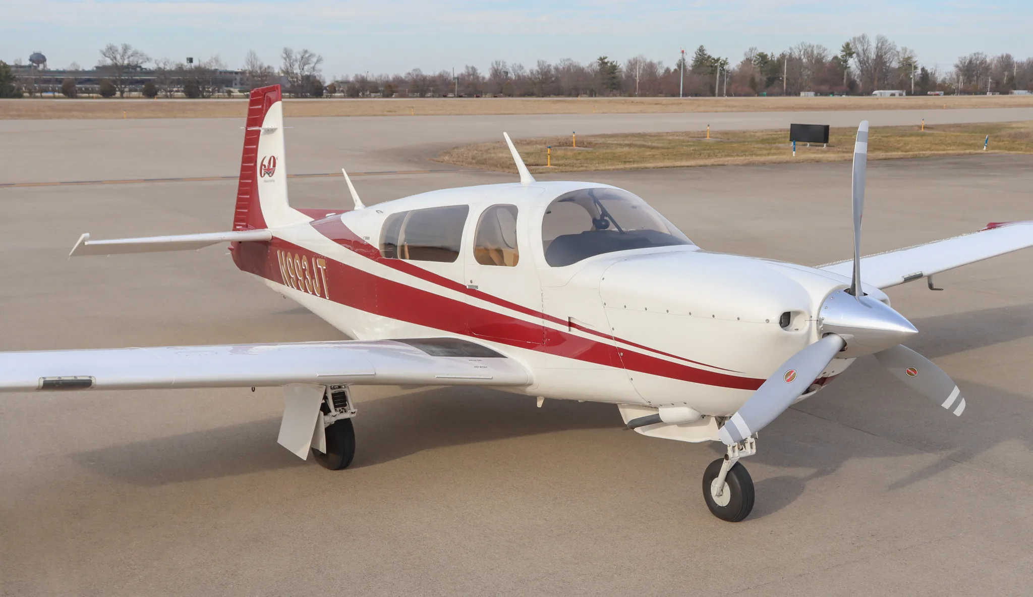Top-down three-quarter view of a white and red single-engine propeller aircraft, N993JT, on an airfield.