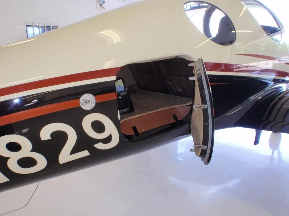 A close-up view of the open baggage compartment on the side of the N829SJ Lancair Evolution aircraft.