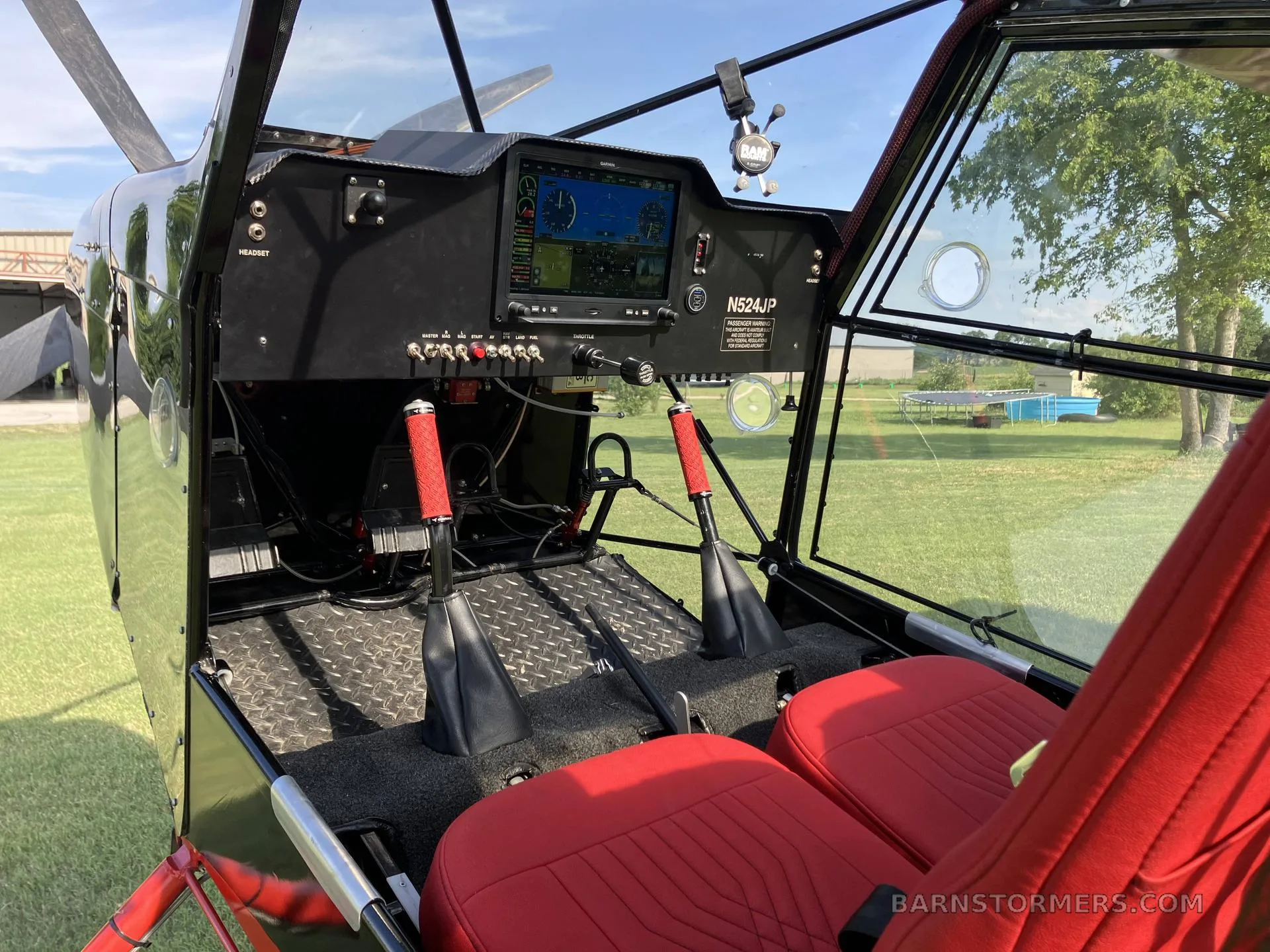 The cockpit of a black and red aircraft, showing the instrument panel, red seats, and control sticks.