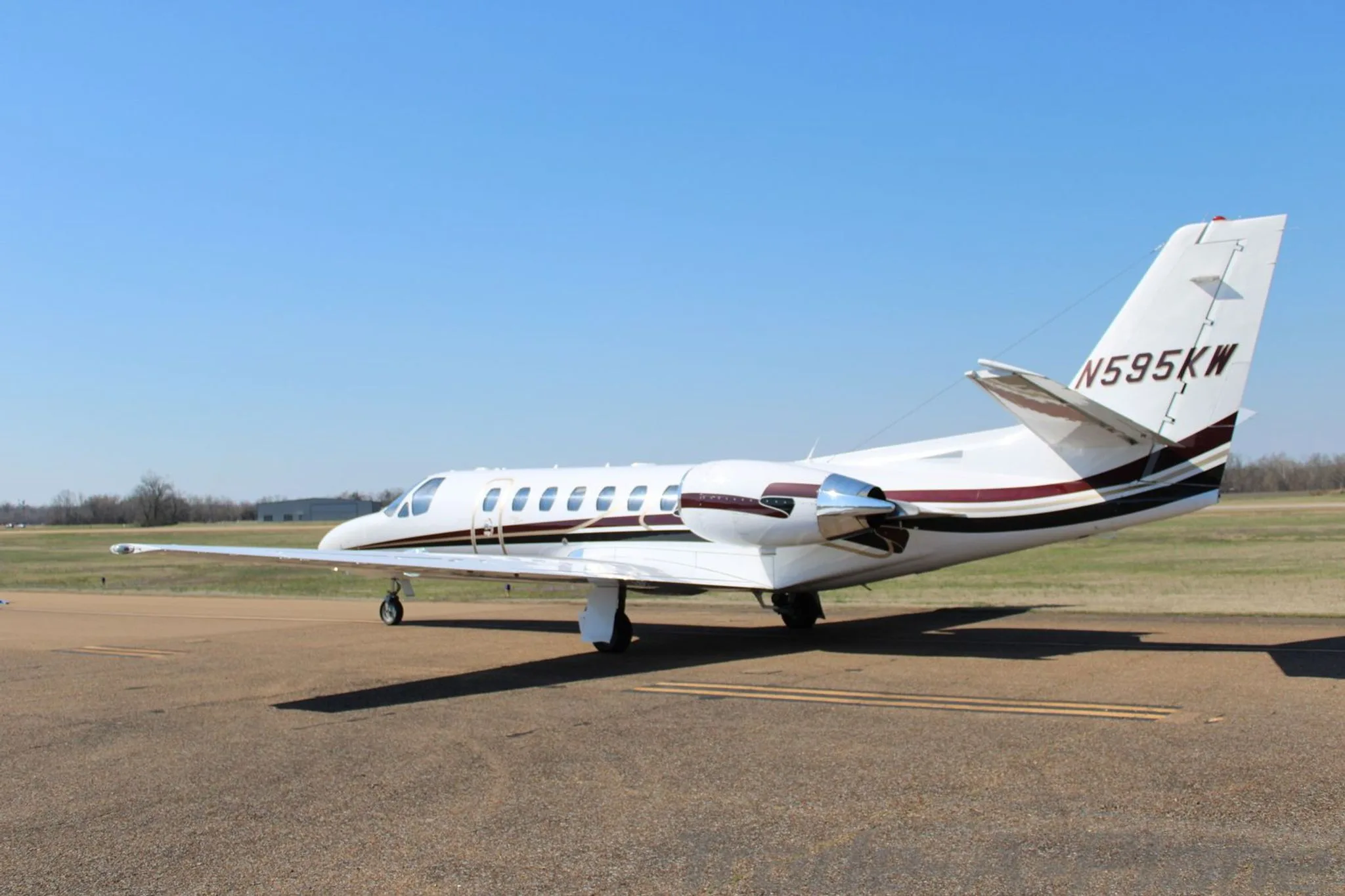 A three-quarter rear view of a white Cessna Citation Encore business jet with dark brown and gold stripes on the tarmac.