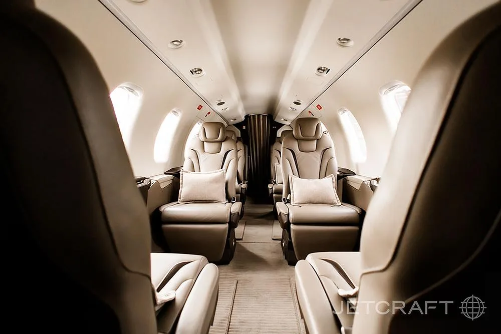 View down the aisle of a luxurious aircraft cabin with tan leather seats and small pillows.