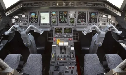 A modern aircraft cockpit is shown with multiple digital displays, control yokes, and a central control panel.