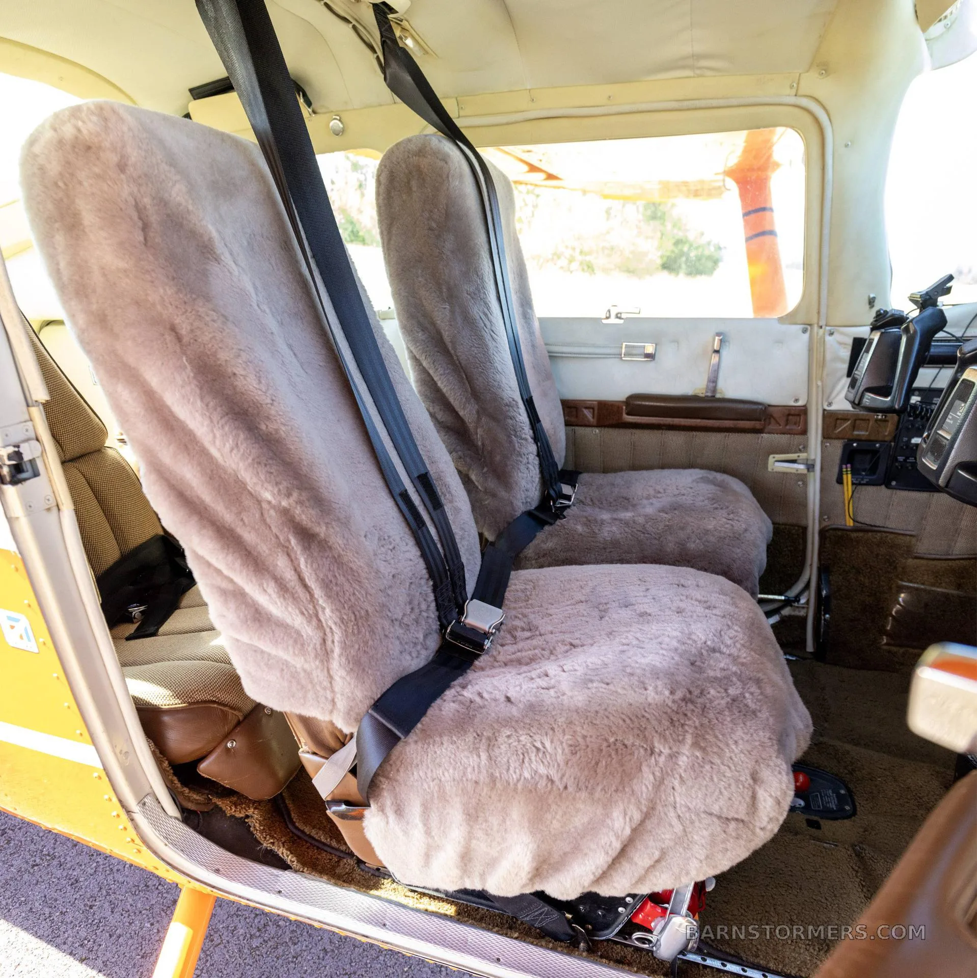 The front cabin of the aircraft features two seats covered with light-colored sheepskin covers and black seatbelts.