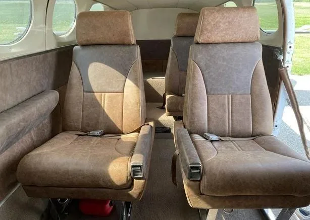 Two rows of brown and tan leather aircraft cabin seats with seatbelts, viewed from the rear of the cabin.