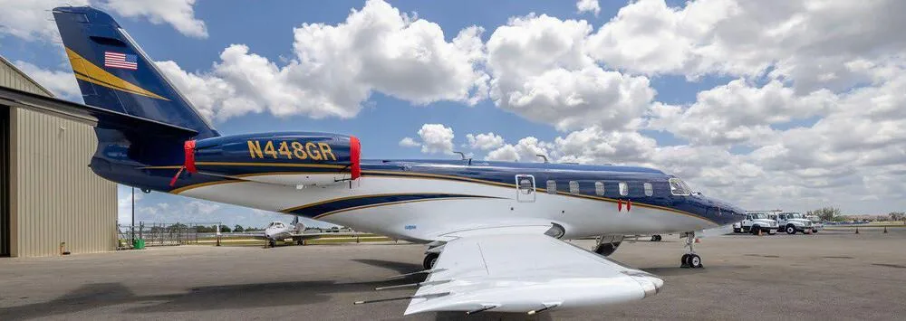A blue and white business jet, N448GR, with gold stripes parked on an airfield, viewed from the rear-left.