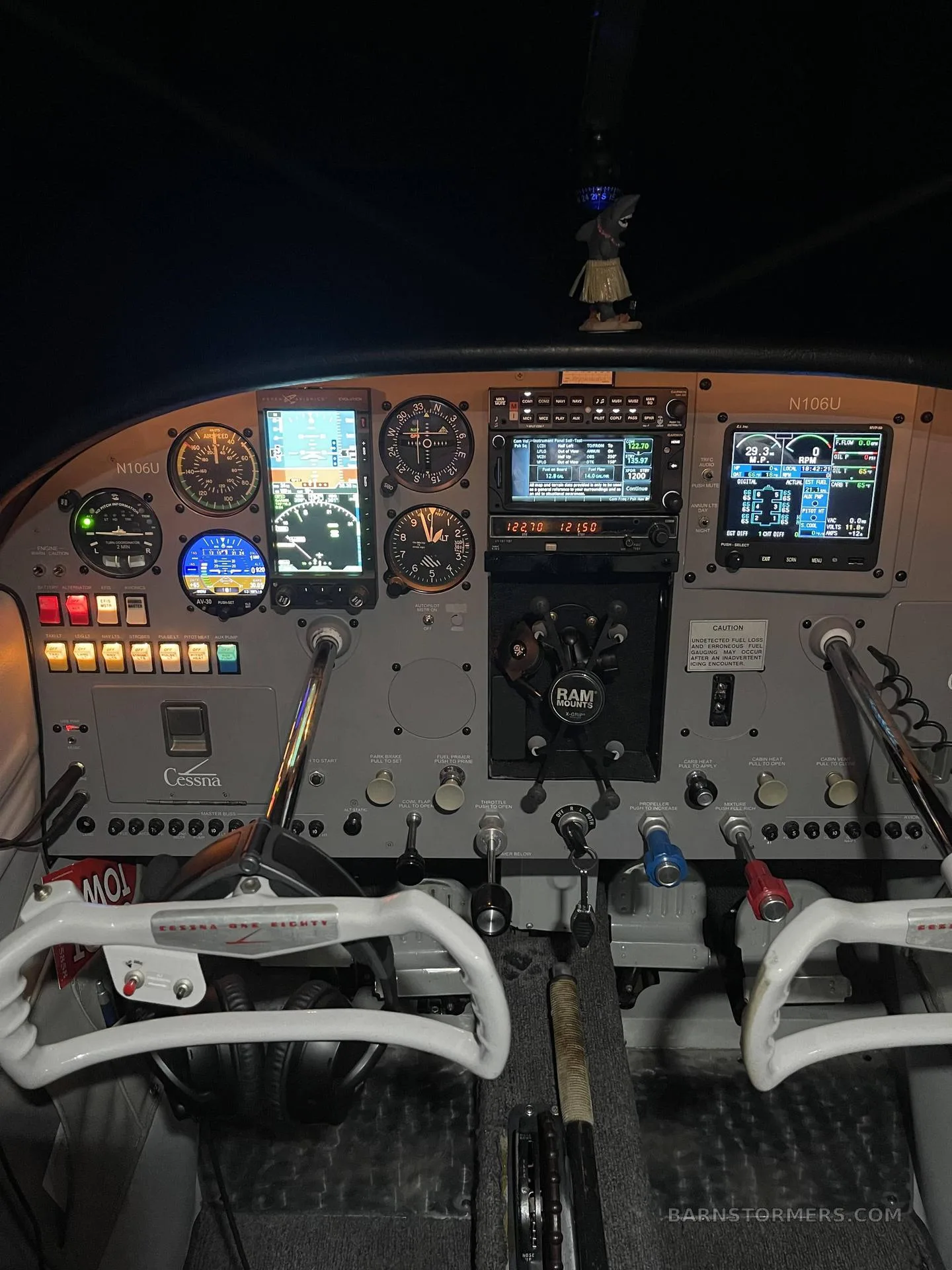 The illuminated cockpit of a Cessna 182 (N106U) features a modern avionics panel with multiple digital displays and traditional gauges.