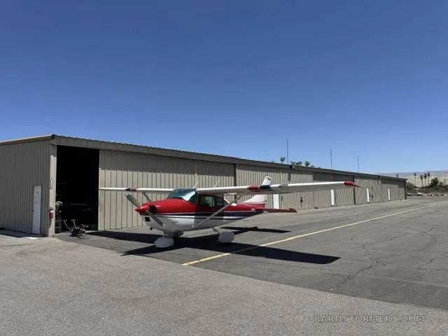 A red, white, and blue single-engine propeller aircraft parked on an asphalt ramp in front of a hangar.