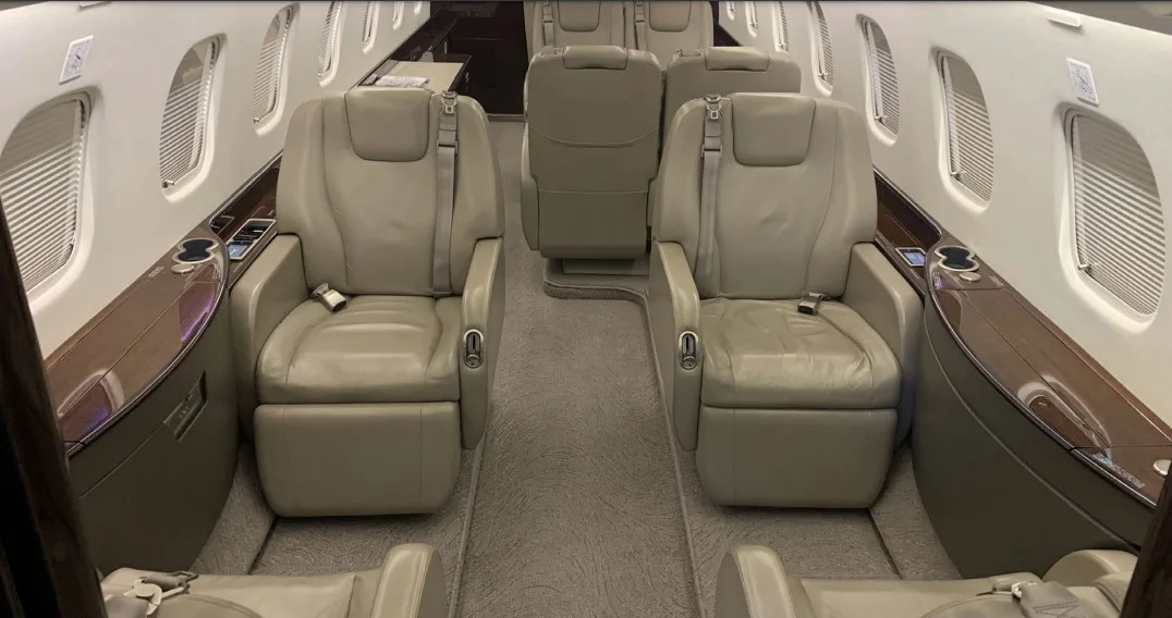 A view down the aircraft cabin aisle, showing two rows of beige leather seats and dark wood paneling.