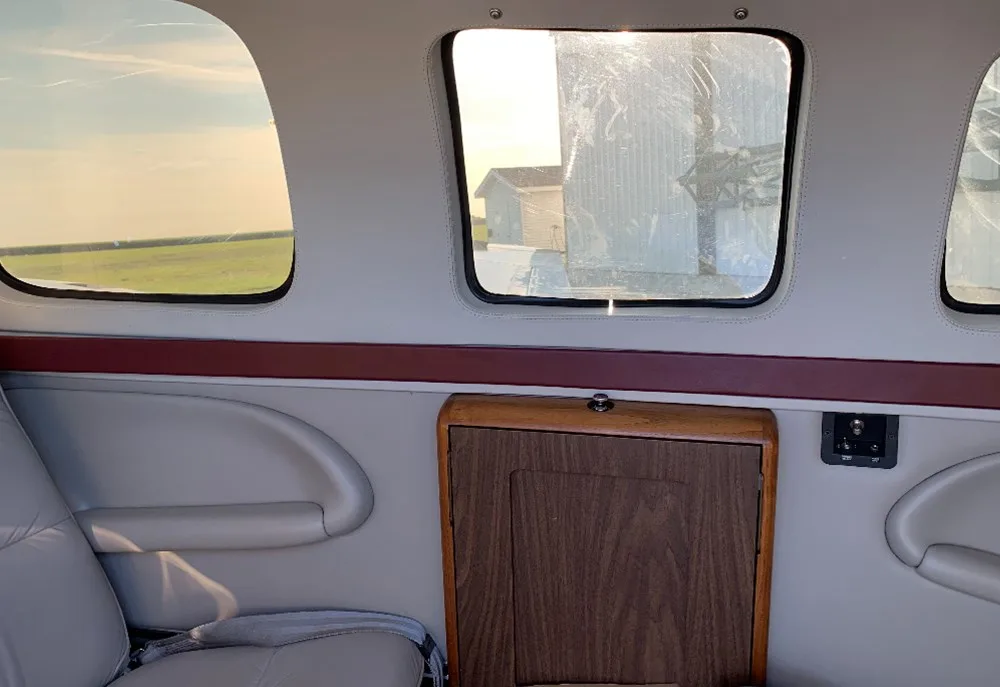 A view of the aircraft cabin interior showing windows, light gray side panels, and a small wooden cabinet.