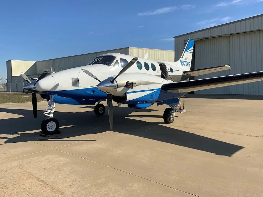 A front-side view of the white and blue twin-engine turboprop aircraft, N579PS, parked on an airfield.