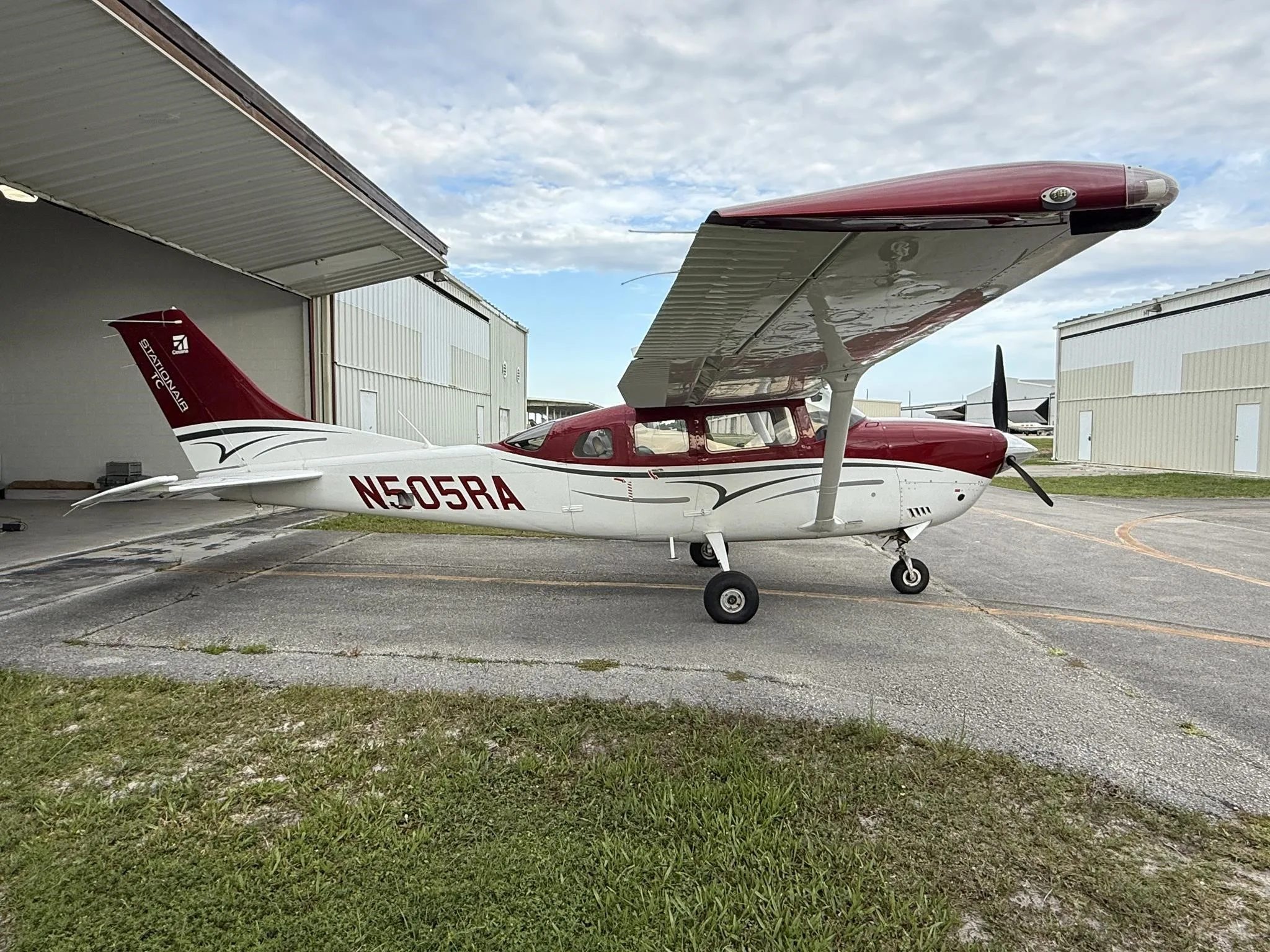 A red and white Cessna Stationair TC aircraft (N505RA) parked partially in a hangar, viewed from the left side.
