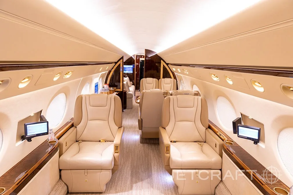 A luxurious aircraft cabin interior with beige leather seats and a central aisle.