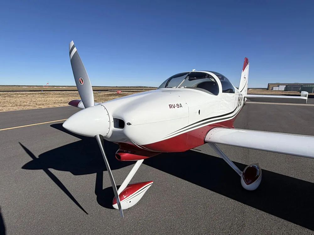 A front-quarter view of the white and red Van's RV-9A aircraft N942R on an airfield, highlighting the propeller and nose.