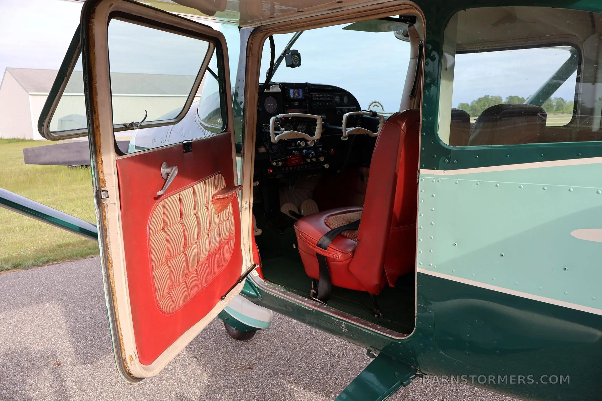 The open door of a green and white aircraft reveals a red upholstered interior and a glimpse of the cockpit.
