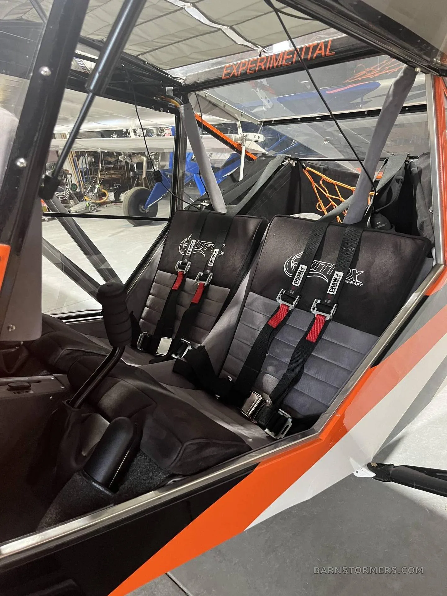 The interior of a Kitfox S7 Super Sport aircraft, showing two black and grey seats with red harnesses and the "EXPERIMENTAL" label.