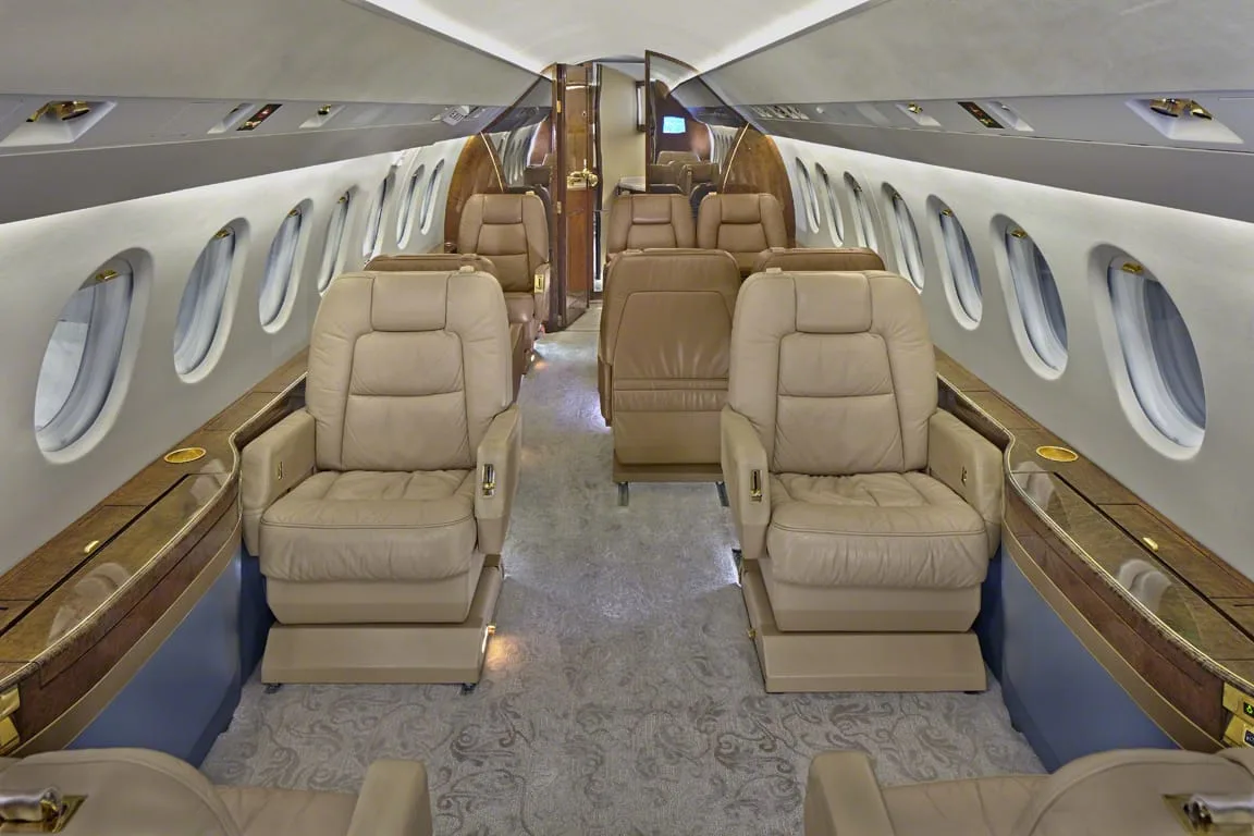 The luxurious cabin interior of a private jet with beige leather seats and a wooden table.