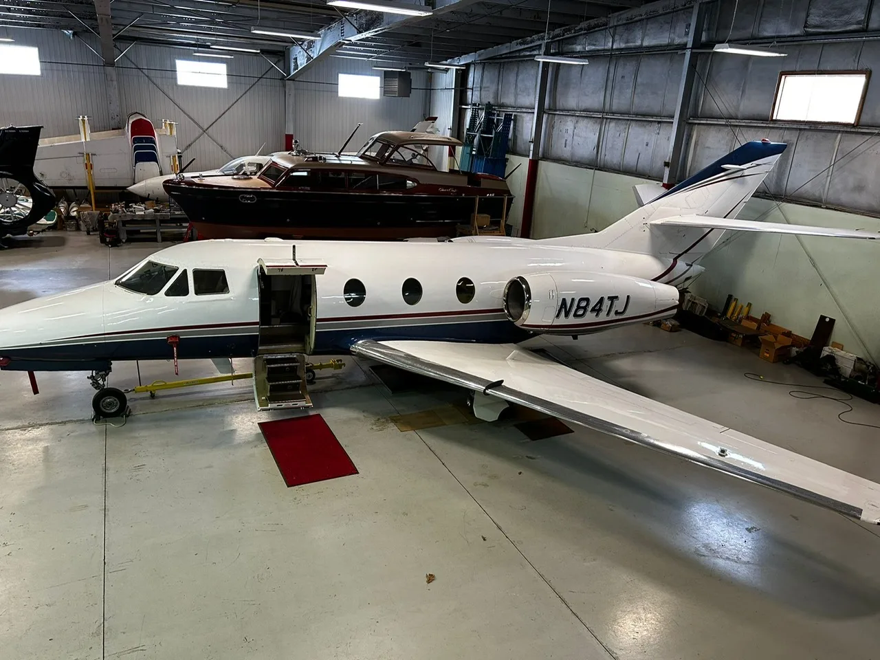 Side view of the aircraft N84TJ in a hangar with the door open.