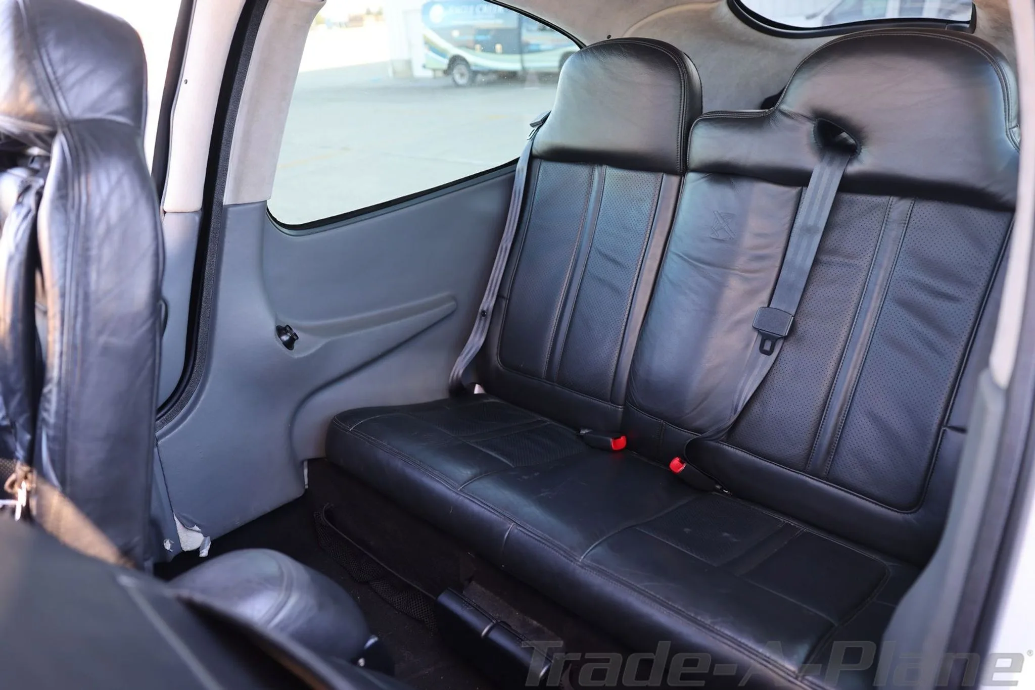 The aircraft's interior showing two black leather rear passenger seats with seatbelts.