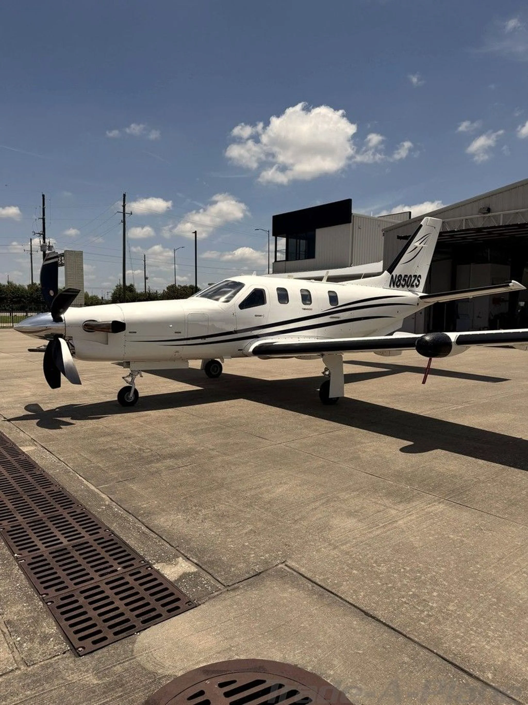 A white turboprop aircraft with black stripes and registration N850ZS parked on an airfield with a hangar in the background.