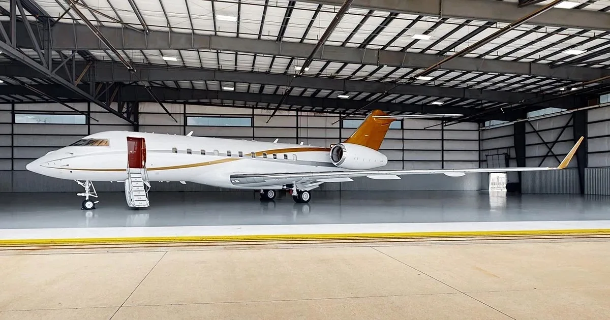 A white business jet with gold accents on the tail and fuselage is parked in a hangar with its main door open and stairs extended.