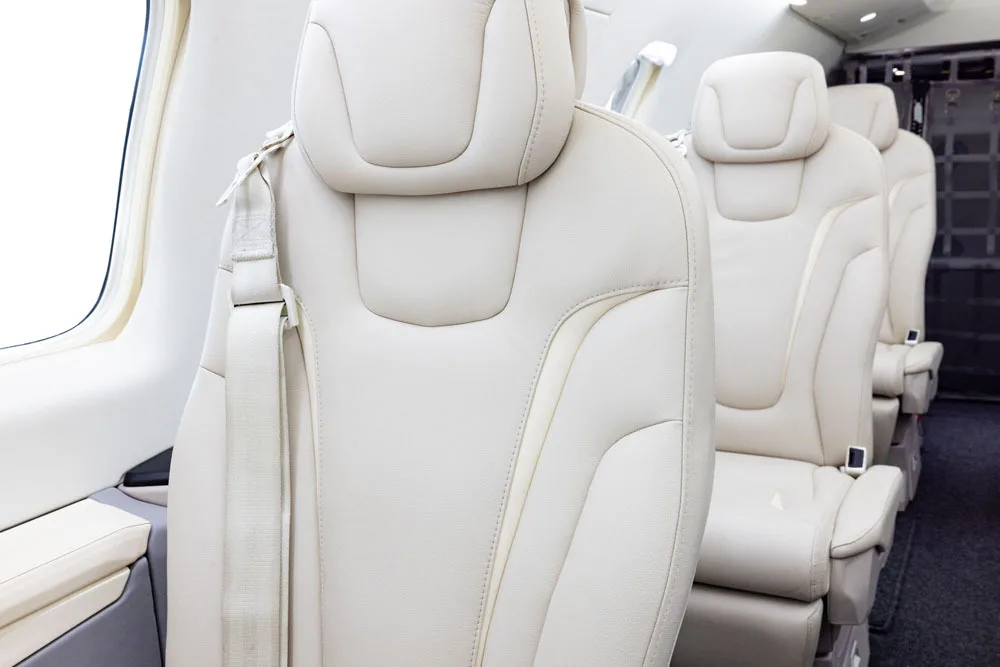 A close-up view of a light beige leather seat in a private jet cabin.