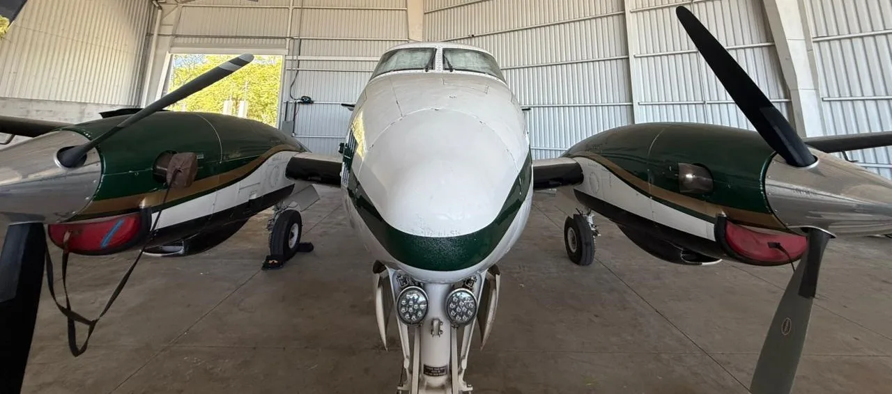 Head-on view of a white and green King Air C90 turboprop aircraft in a hangar.
