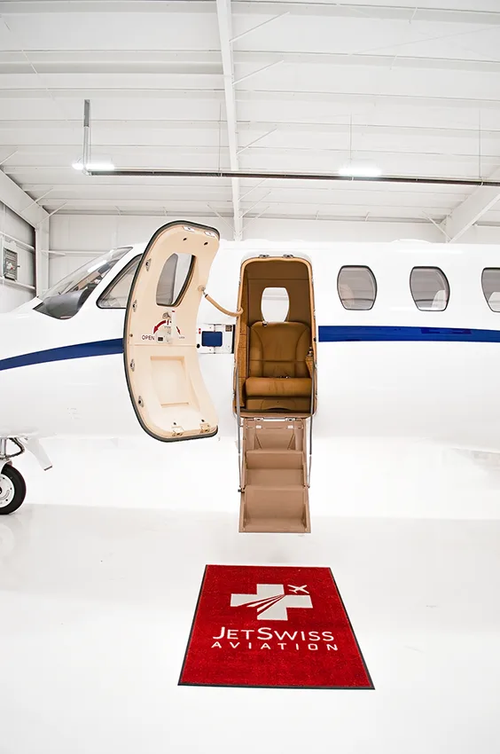The open main cabin door and integrated steps of a white business jet, with a "JetSwiss Aviation" mat on the floor.