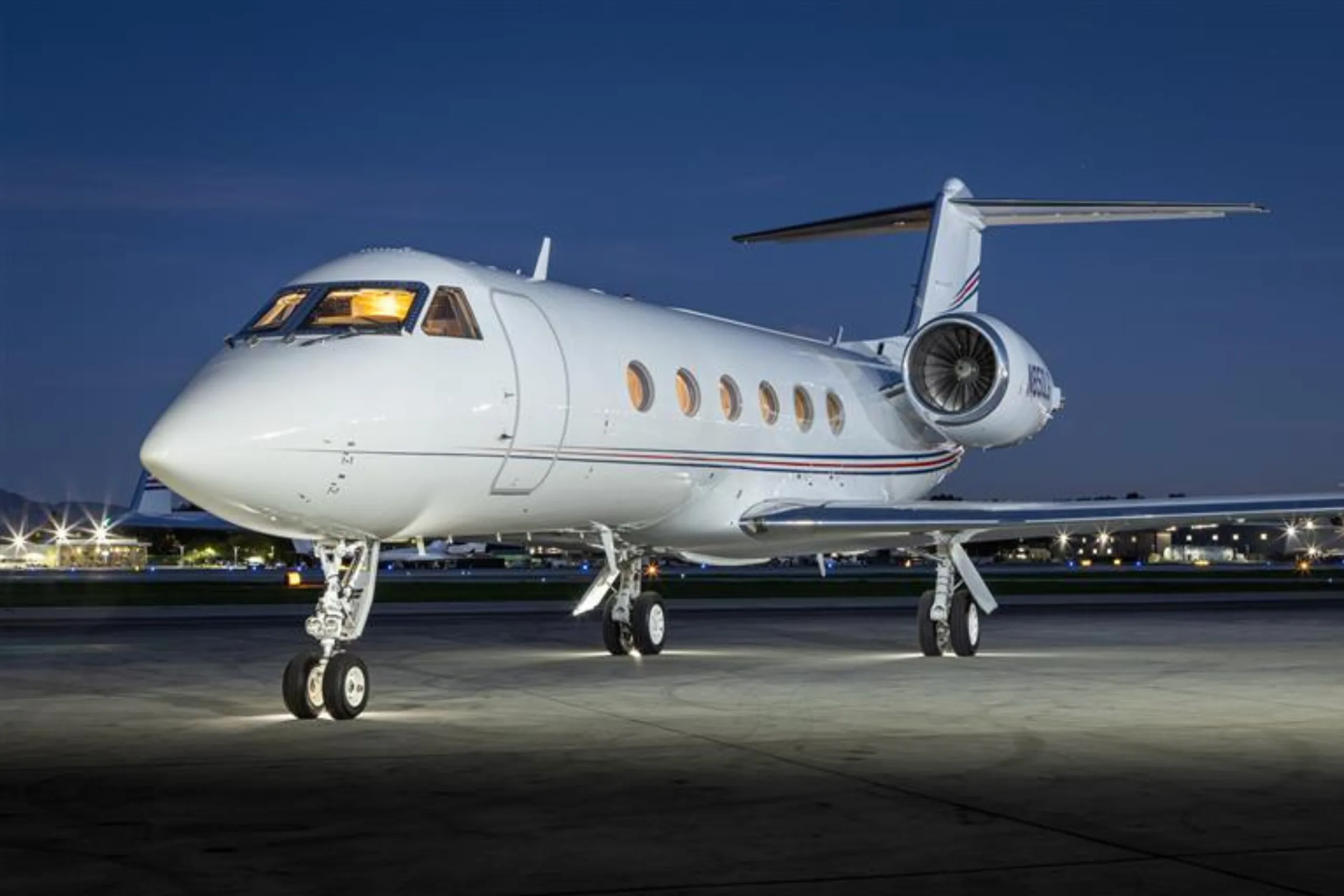 A white private jet is parked on the tarmac at night.