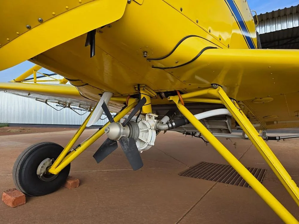 A close-up view of the underside of a yellow agricultural aircraft, showing its spray pump and landing gear.