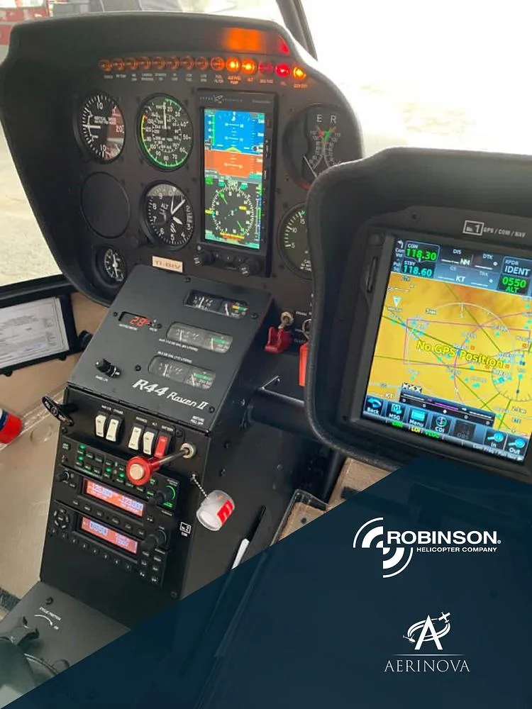 The cockpit of a Robinson R44 Raven II helicopter, showing the instrument panel, radios, and two display screens.