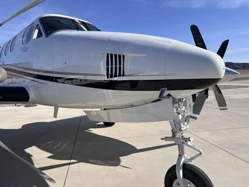 A close-up of the front-left fuselage and landing gear of the white and black turboprop aircraft.