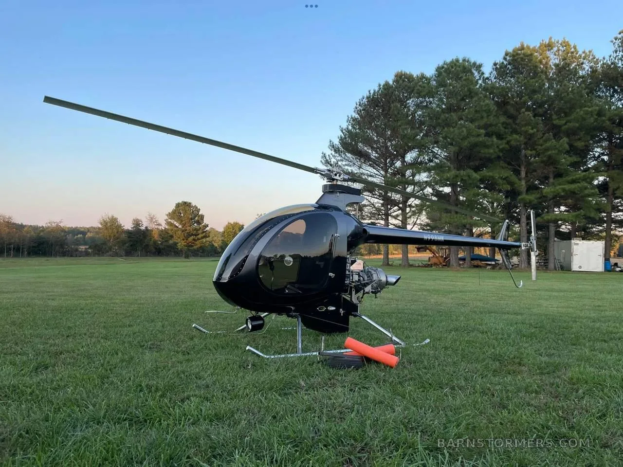 A black single-seat helicopter with an exposed engine sits on a grassy field under a clear sky.