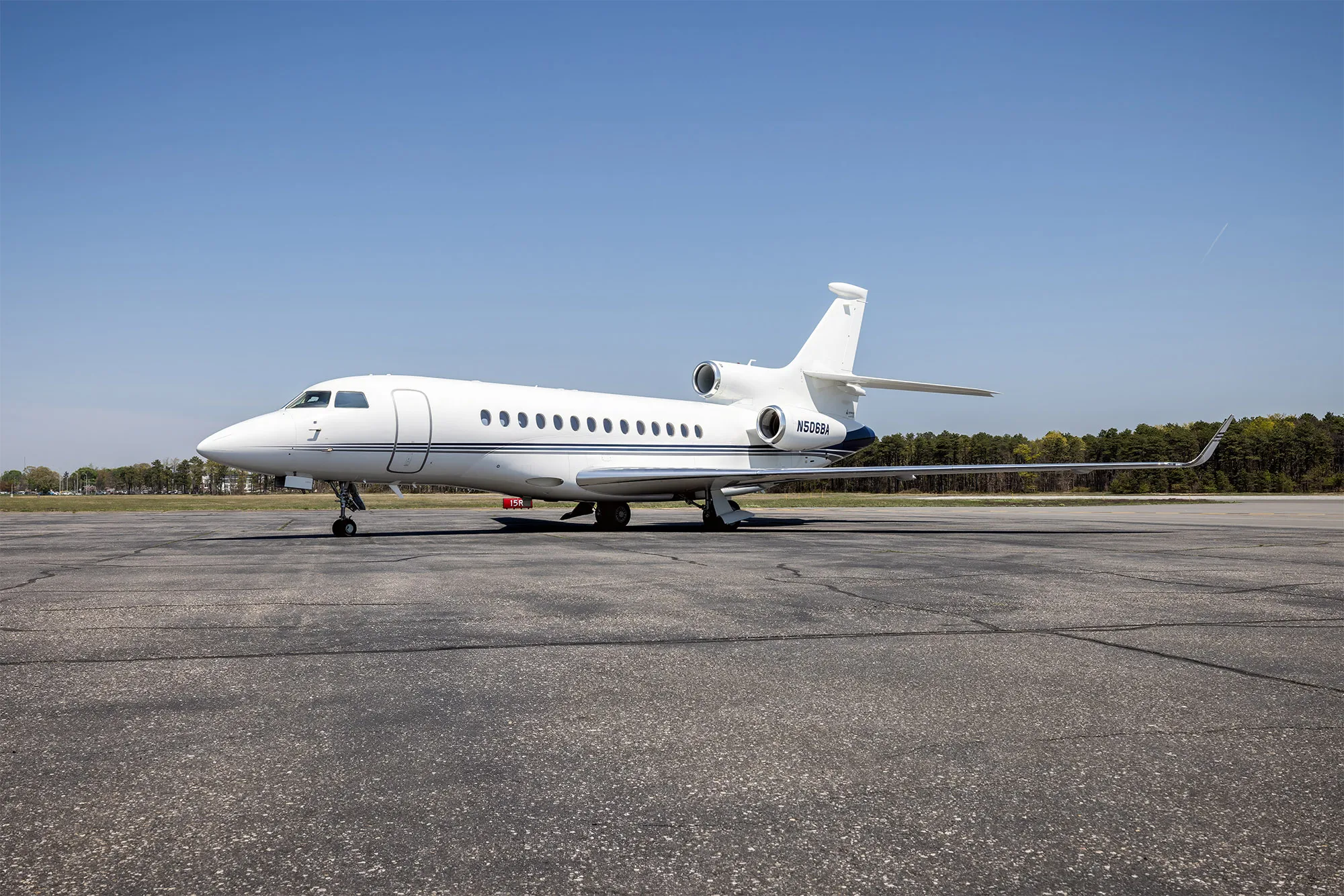 A white Dassault Falcon 900EX business jet with blue accents on the tail, parked on an asphalt tarmac under a clear blue sky.