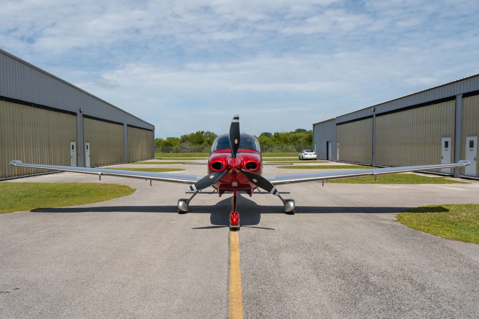 Front view of a red and silver Cirrus SR22 GTS parked on an airfield between hangars.